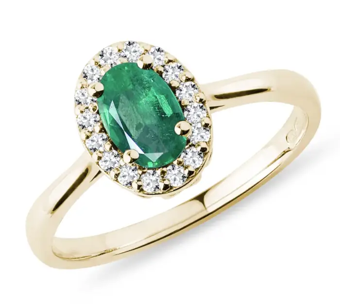Oválný halo prsten ze žlutého 14k zlata s centrálním smaragdem, kolem kterého jsou usazeny čiré brilianty